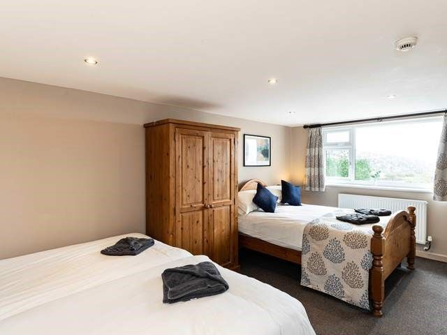 A bedroom showing 3 single beds and a pine wardrobe with a large window behind.