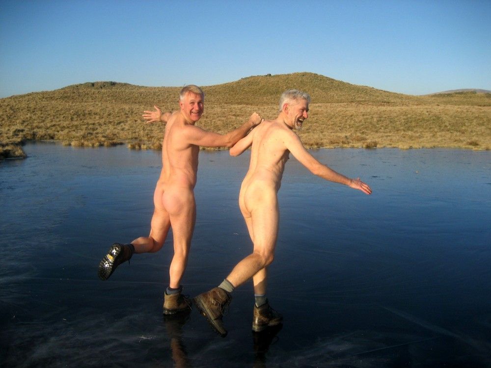 Two naked men skating on a lake