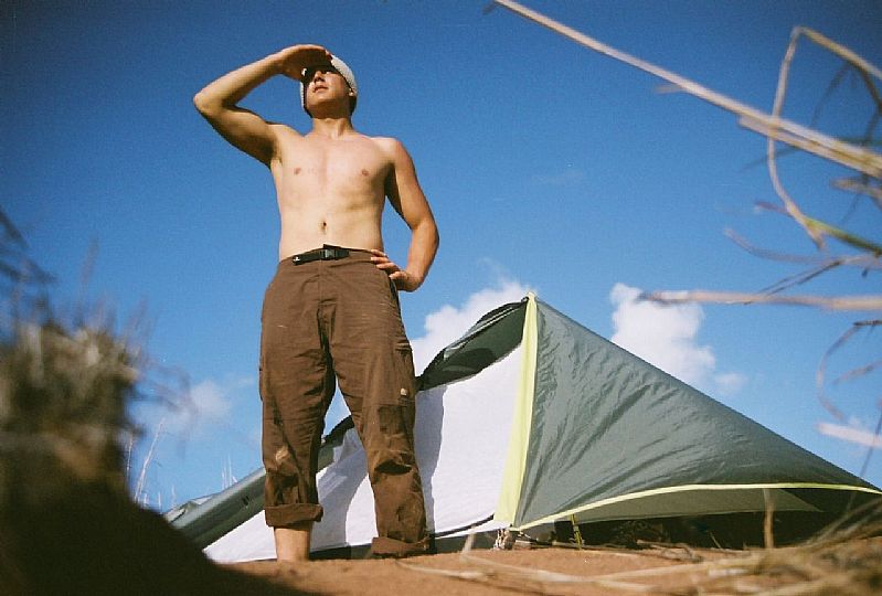 Photo of a topless man scanning the horizon in front of a tent