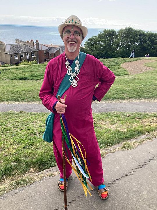 Man dressed in a magenta outfit with a blue sash and an elaborate pearl necklace